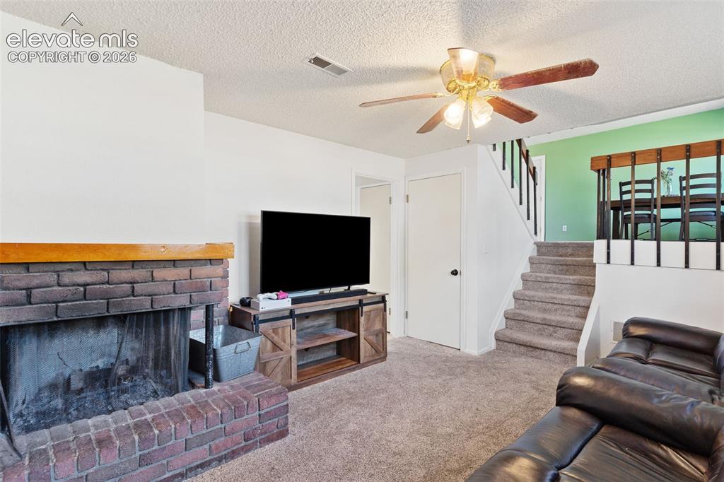 Image 24 of 36: Living area featuring a brick fireplace with a wood mantle, carpet flooring