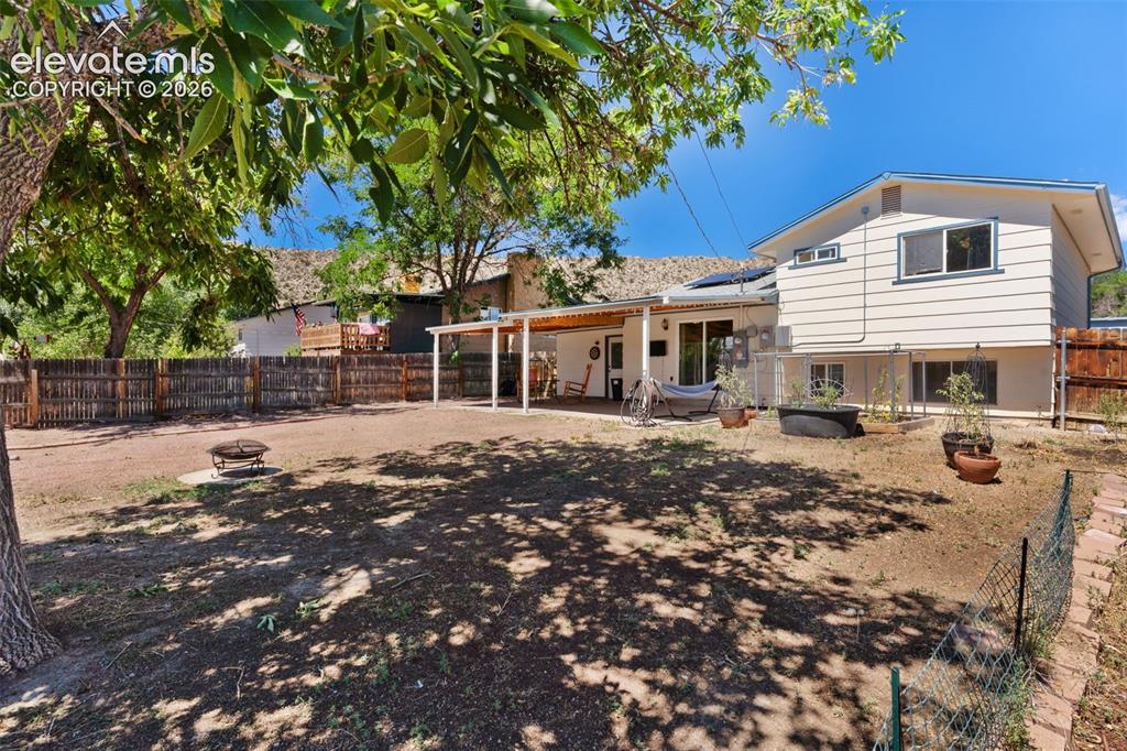 Image 36 of 36: Spacious backyard featuring a covered patio, a fire pit area, and mature tr