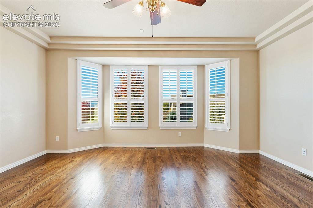 Image 19 of 50: Room featuring wood-finish flooring, tray ceilings, a bay window with white