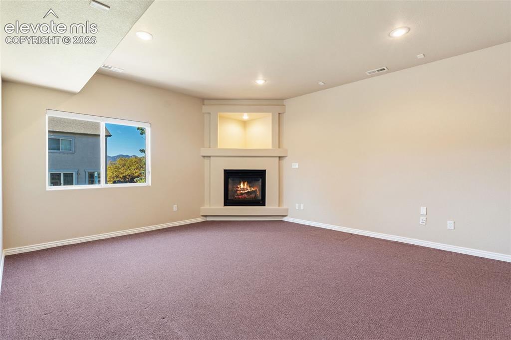 Image 32 of 50: Corner fireplace featuring a built-in recessed shelf, carpeted flooring, sl