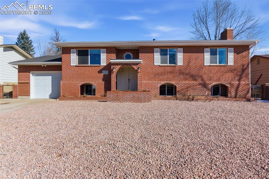 Image 3 of 50: View of front of property featuring brick siding, a chimney, an attached ga