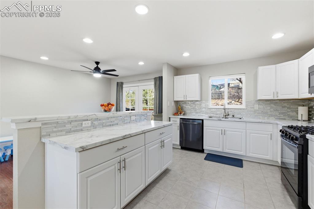 Image 7 of 50: Kitchen with black gas range, white cabinets, tasteful backsplash, stainles