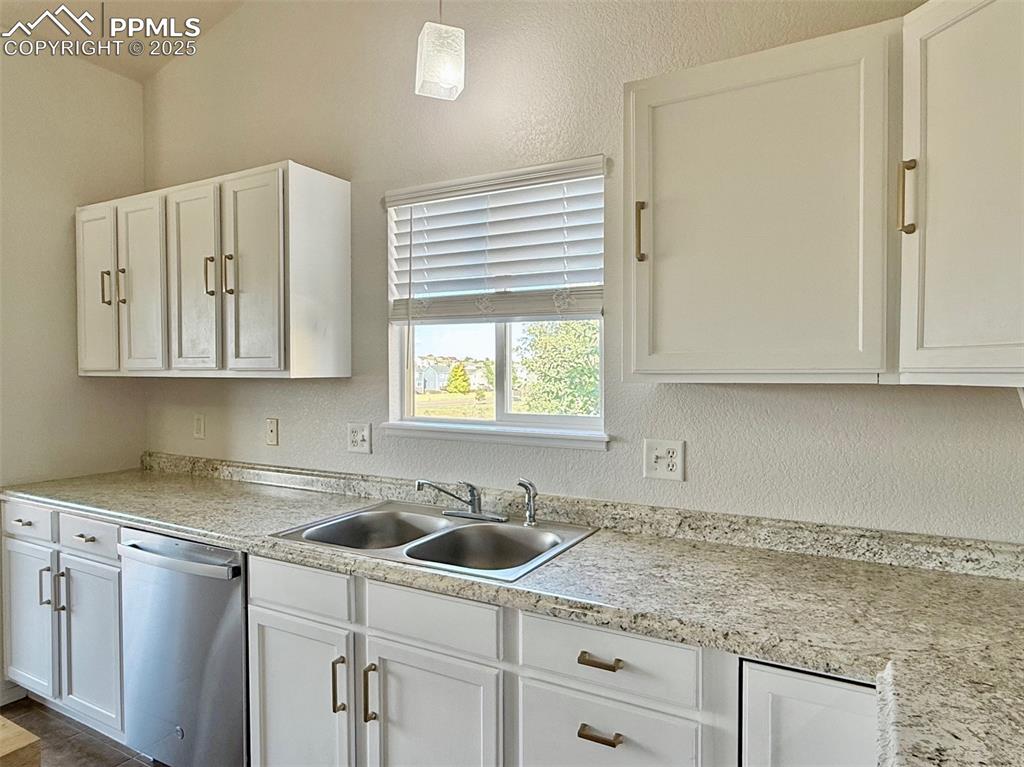 Image 10 of 37: Kitchen with stainless steel dishwasher, white cabinets, and hanging light