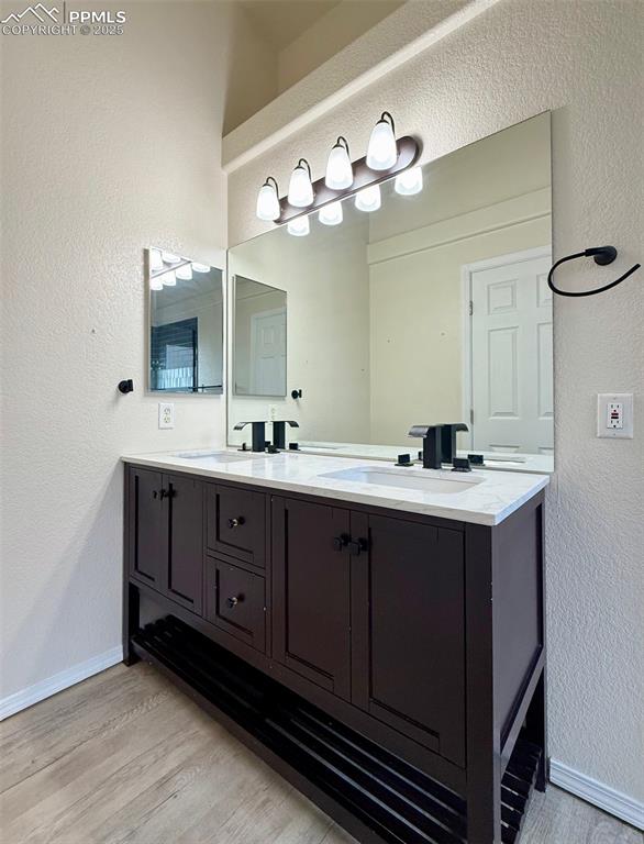 Image 16 of 37: Full bathroom with a textured wall, double vanity, and light wood-style flo
