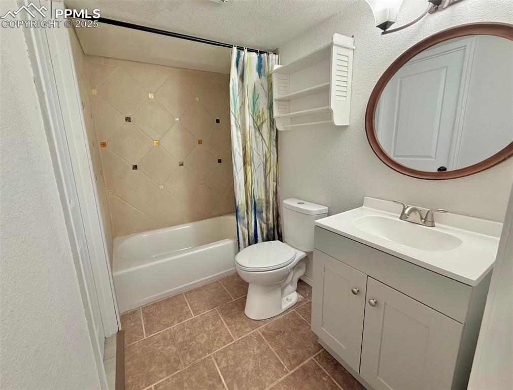 Image 32 of 37: Bathroom featuring a textured wall, shower / bathtub combination with curta