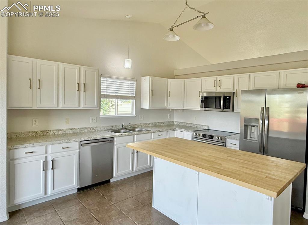 Image 9 of 37: Kitchen with pendant lighting, white cabinetry, stainless steel appliances,
