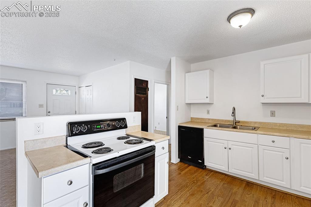 Image 12 of 19: Kitchen with electric range, light countertops, white cabinetry, a textured