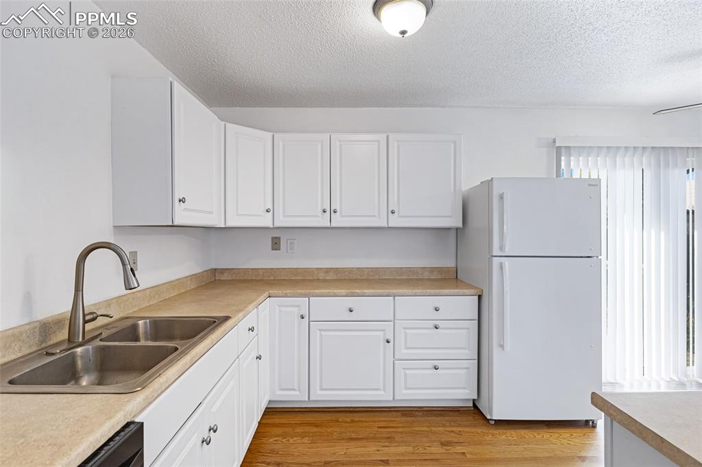 Image 13 of 19: Kitchen with freestanding refrigerator, light countertops, white cabinets, 