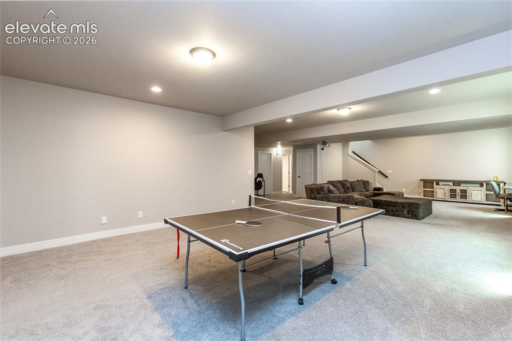 Image 28 of 43: Expansive room with neutral carpet, recessed lighting, and a visible stairc