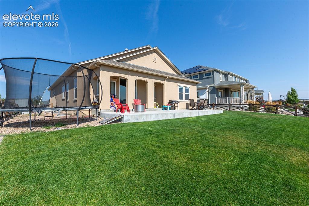 Image 35 of 43: Expansive green lawn with a concrete patio featuring a built-in fire pit, m