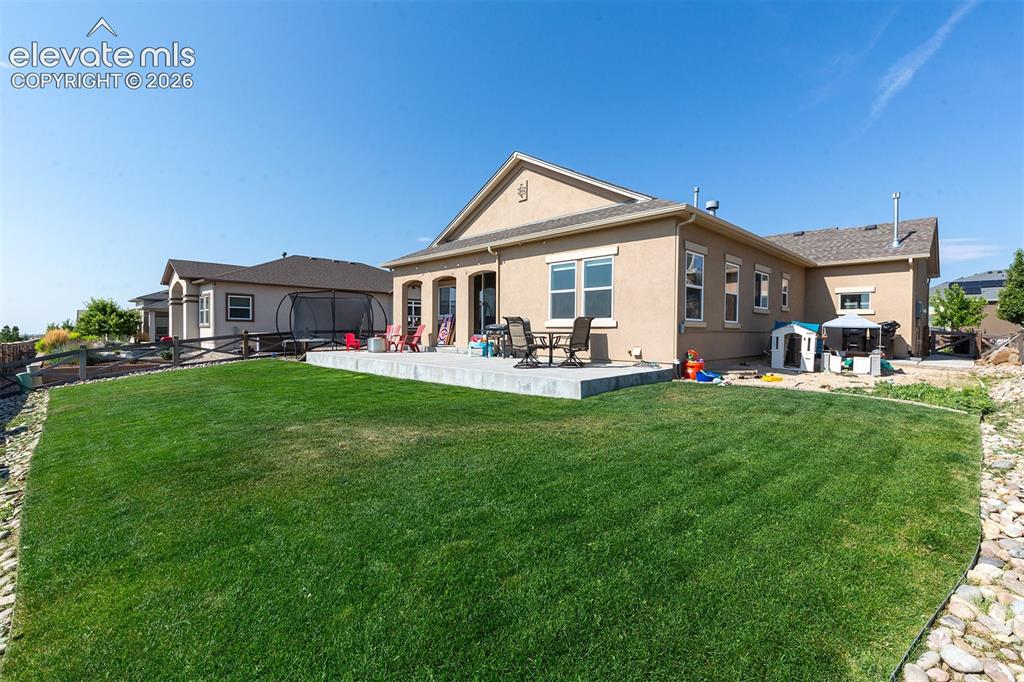 Image 36 of 43: Expansive rear lawn with a level concrete patio, stucco exterior, and multi