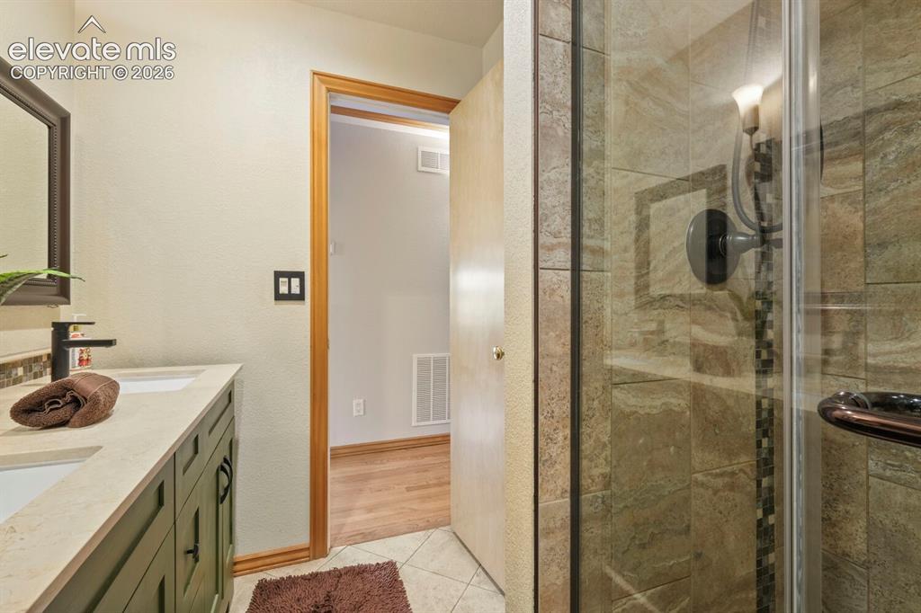 Image 21 of 50: Dual vanity with green cabinetry, integrated sinks, and matte black fixture