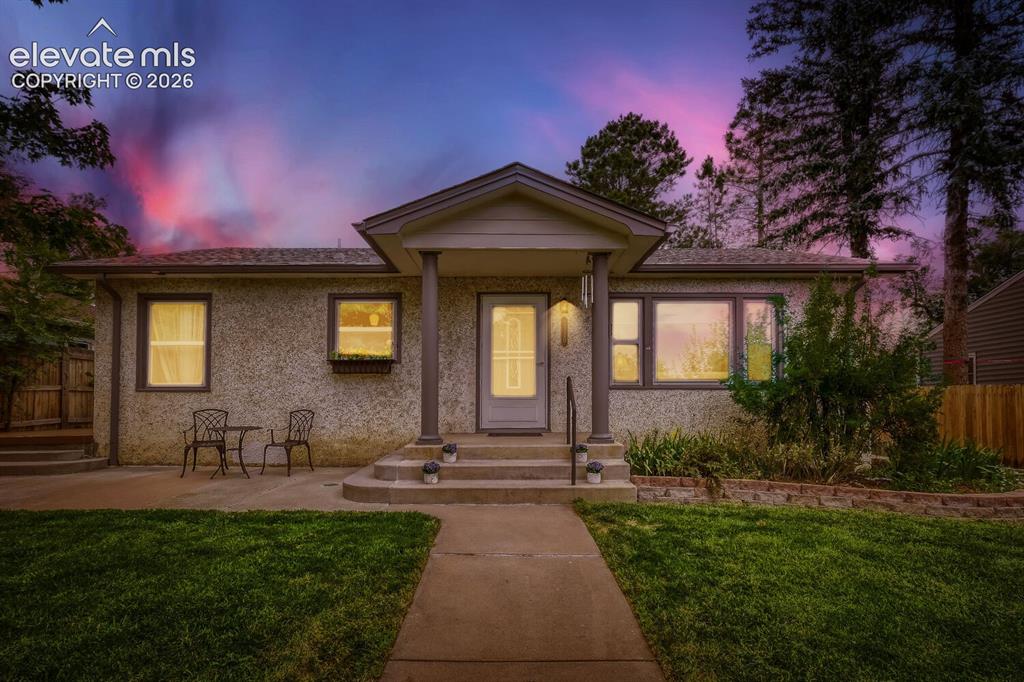 Image 3 of 50: Elevated front yard featuring a manicured lawn, established trees, and a wr