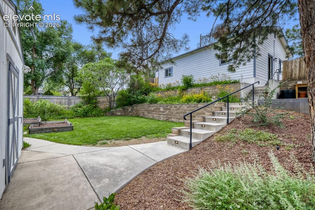 Image 33 of 50: Expansive backyard featuring a raised garden bed, stone retaining walls, an