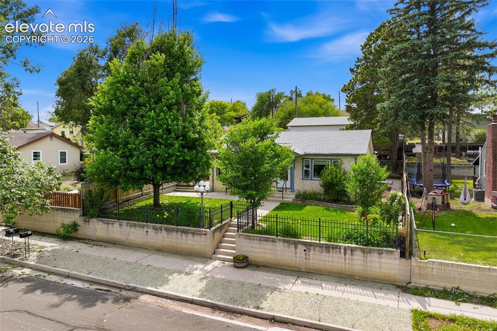 Image 37 of 50: Elevated front yard featuring a manicured lawn, established trees, and a wr