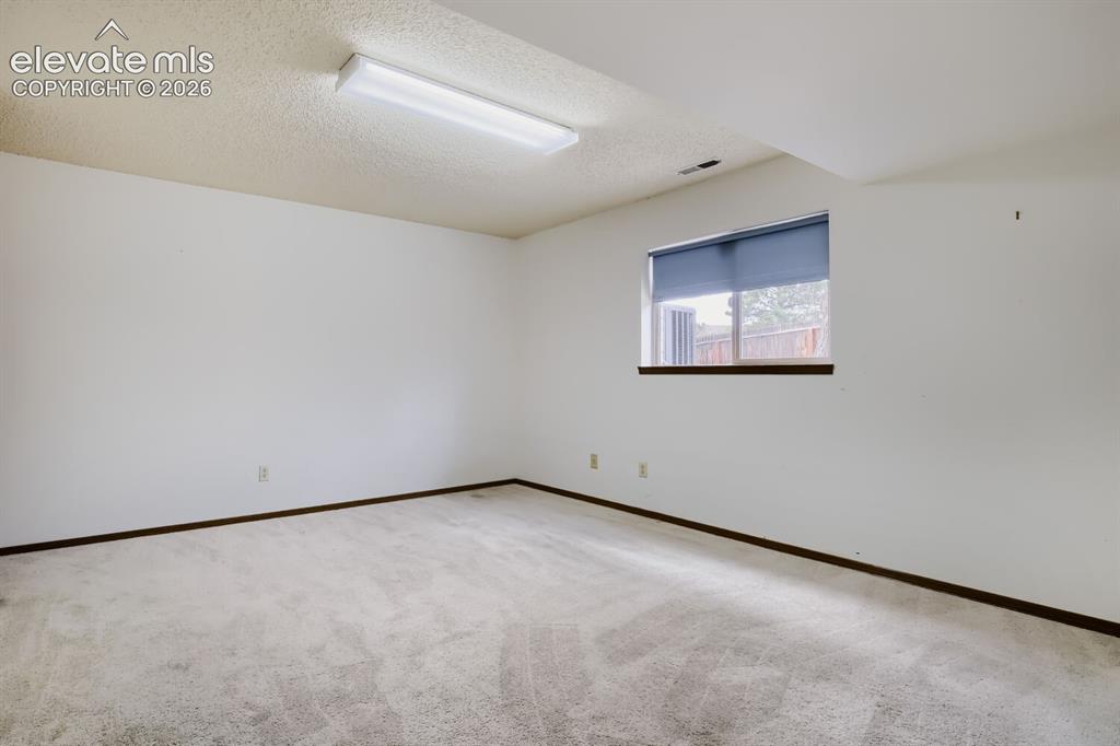 Image 20 of 28: Carpeted room featuring a single window with blinds, white walls, dark base