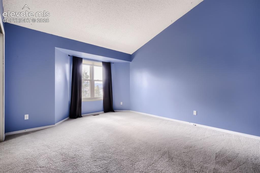 Image 9 of 28: Spacious room featuring vaulted ceilings, a large bay window, light grey ca