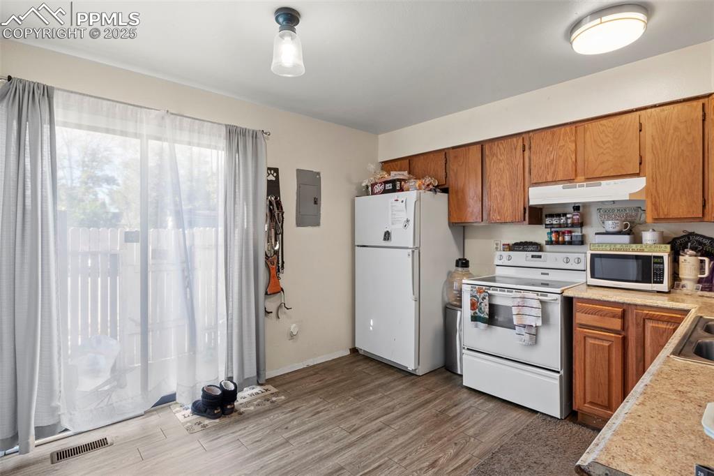 Image 11 of 31: Kitchen featuring light countertops, brown cabinetry, white appliances, lig
