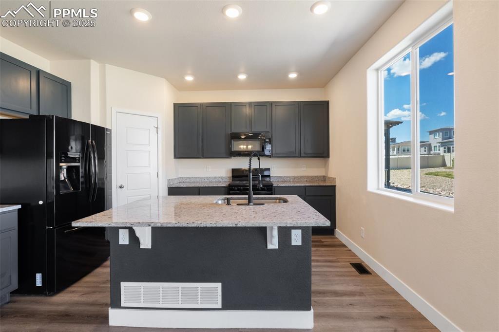 Image 10 of 35: Kitchen with black appliances, light stone counters, a breakfast bar area,