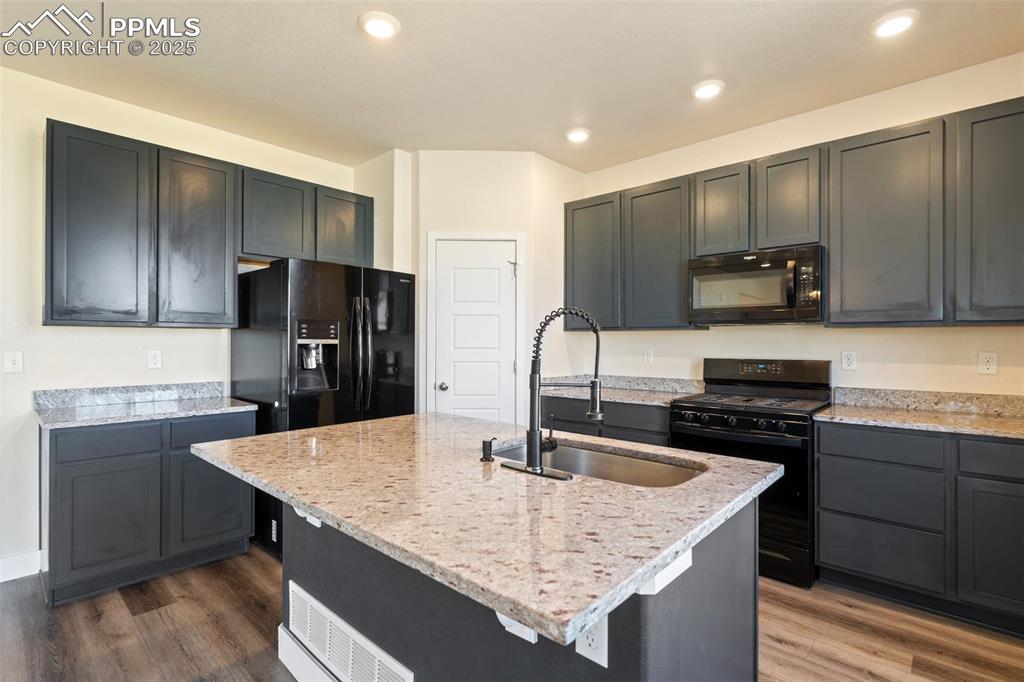 Image 11 of 35: Kitchen featuring black appliances, light stone countertops, dark wood-styl