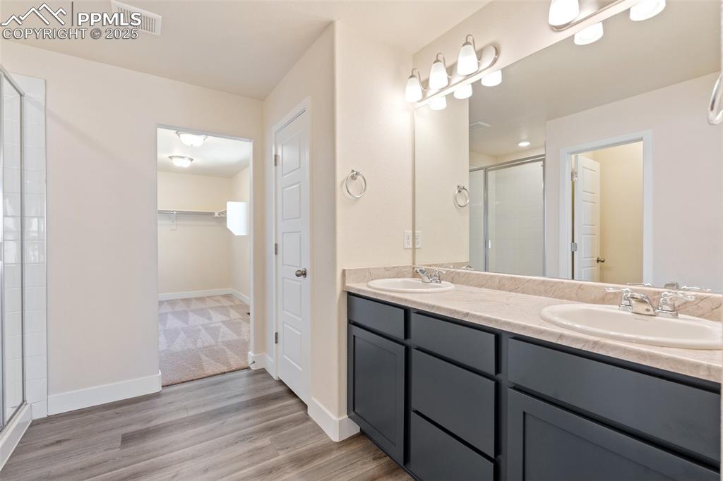 Image 20 of 35: Bathroom featuring a shower stall, a walk in closet, double vanity, and woo
