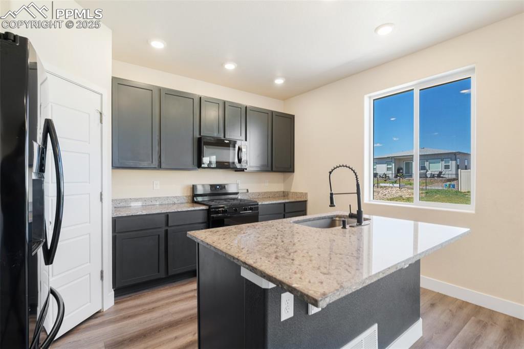 Image 9 of 35: Kitchen featuring black appliances, light wood finished floors, light stone