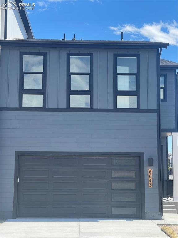 Caption: View of front of home with concrete driveway, board and batten siding, and a garage