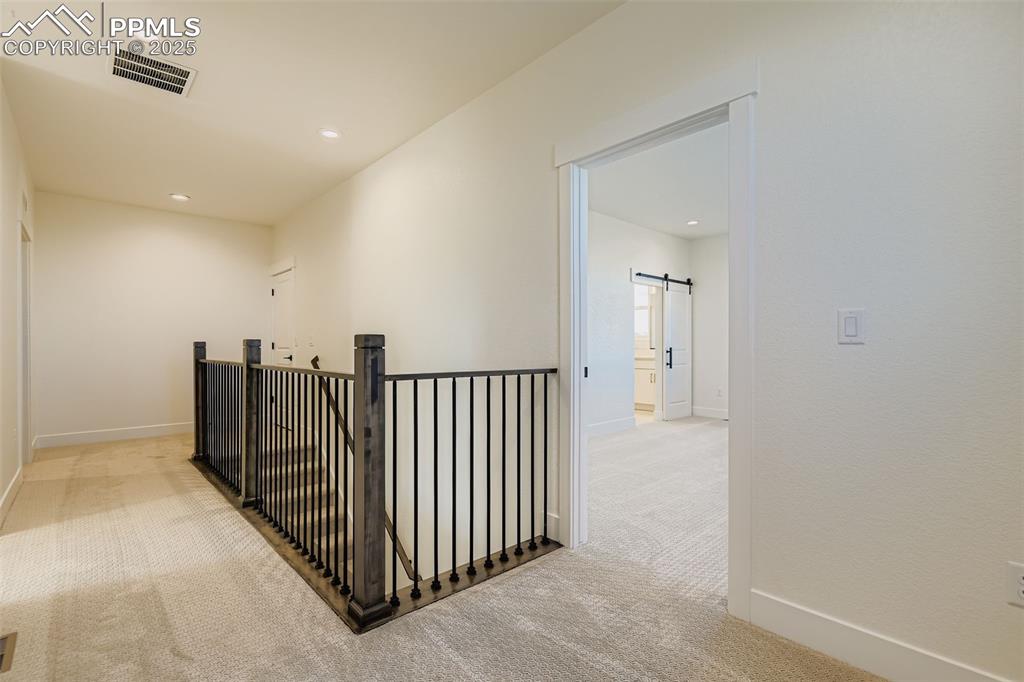 Image 23 of 28: Hall with a barn door, recessed lighting, light carpet, and an upstairs lan