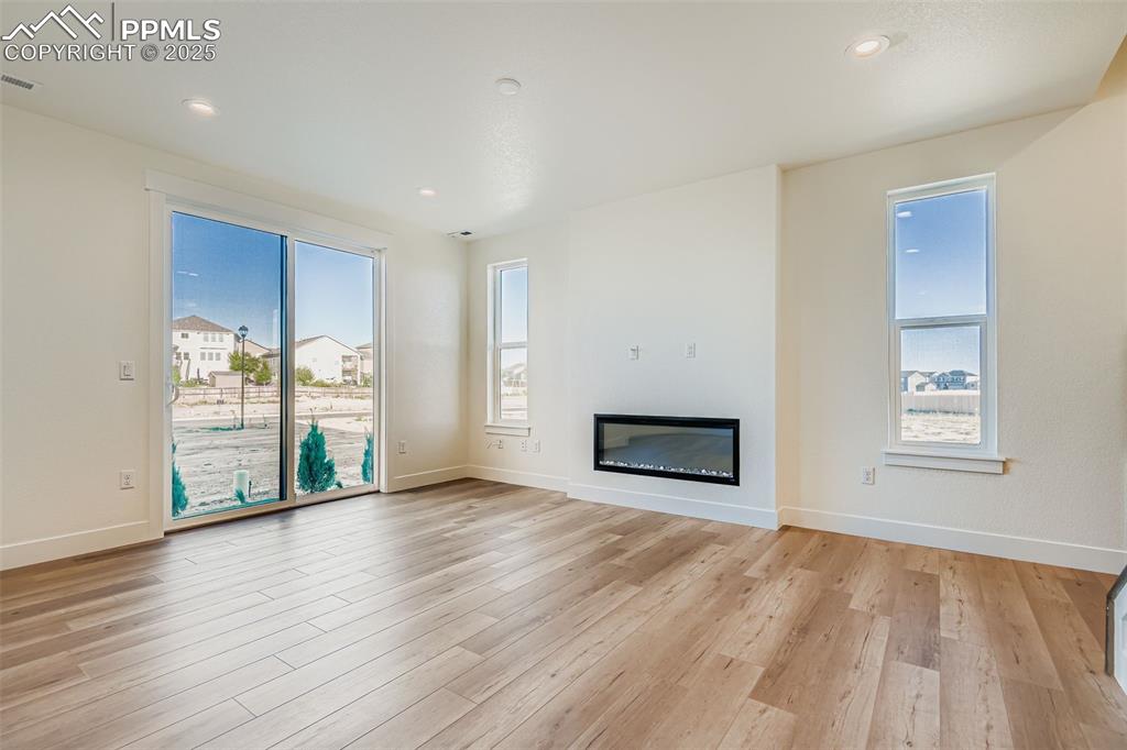 Image 6 of 28: Unfurnished living room featuring a glass covered fireplace, plenty of natu
