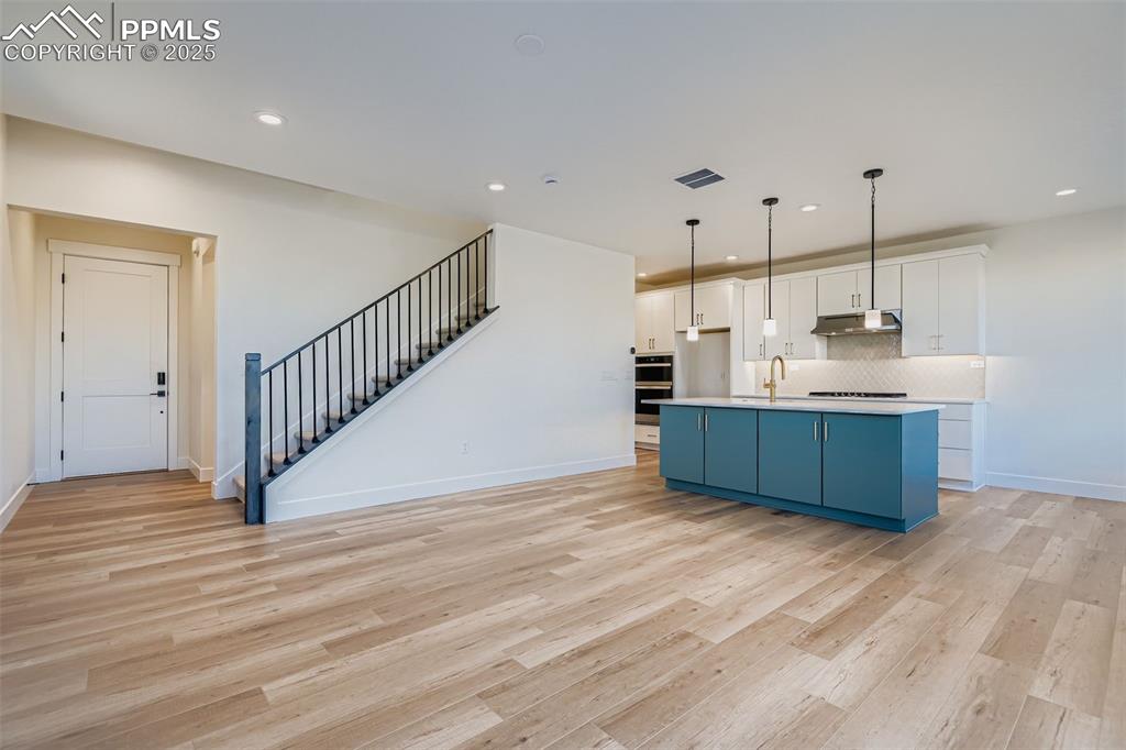 Image 7 of 28: Kitchen featuring blue cabinets, white cabinetry, an island with sink, deco