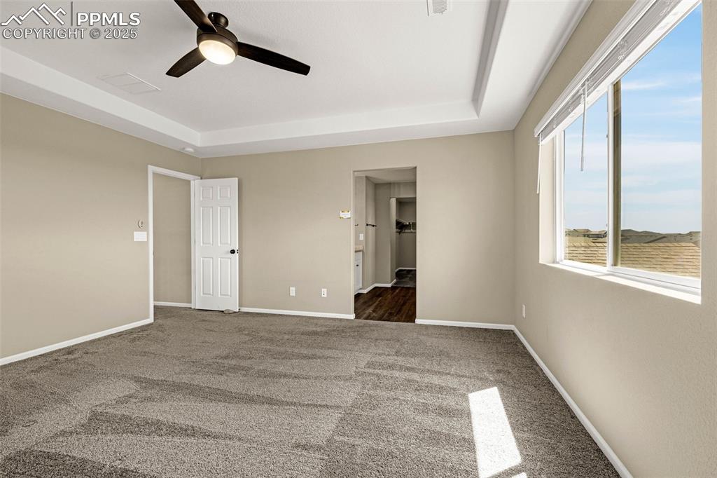 Image 18 of 42: Unfurnished bedroom featuring a tray ceiling, dark carpet, and ceiling fan