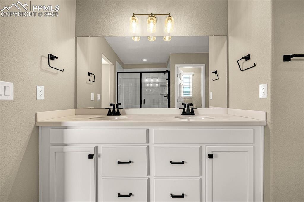 Image 20 of 42: Full bath featuring a textured wall, a shower stall, and double vanity