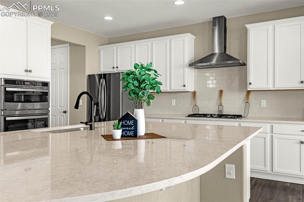 Image 4 of 42: Kitchen featuring wall chimney range hood, white cabinets, decorative backs