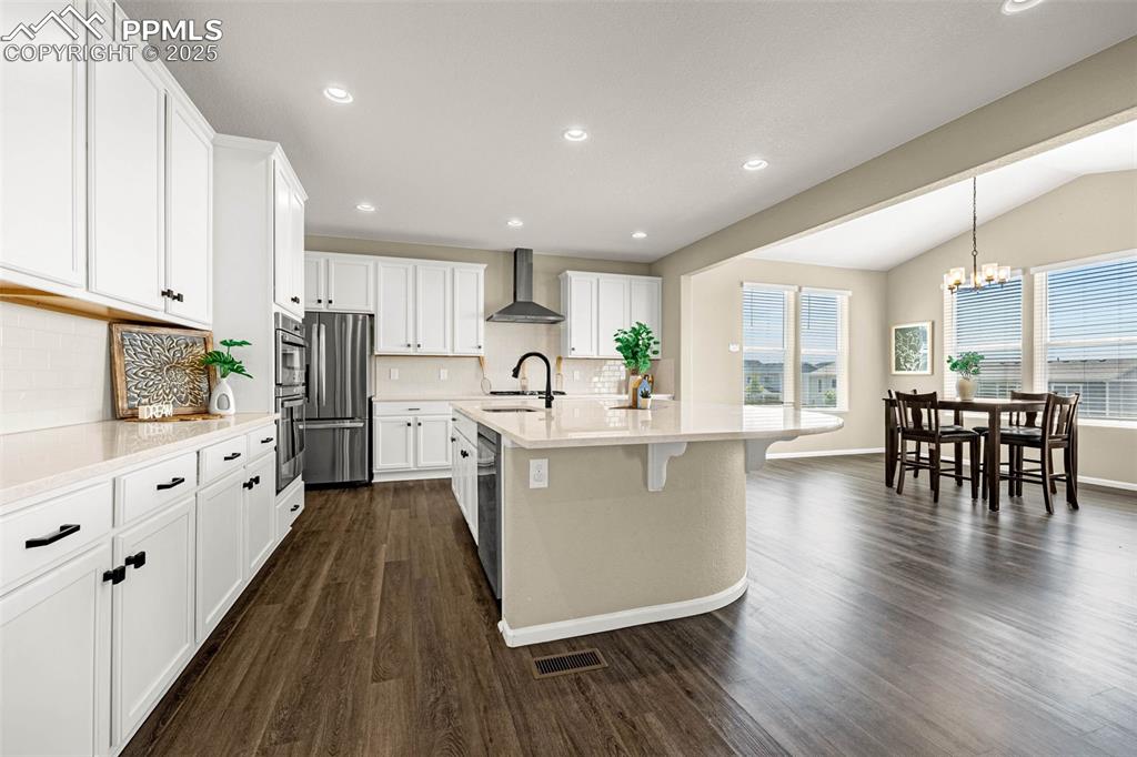 Image 5 of 42: Kitchen featuring vaulted ceiling, white cabinetry, a center island with si