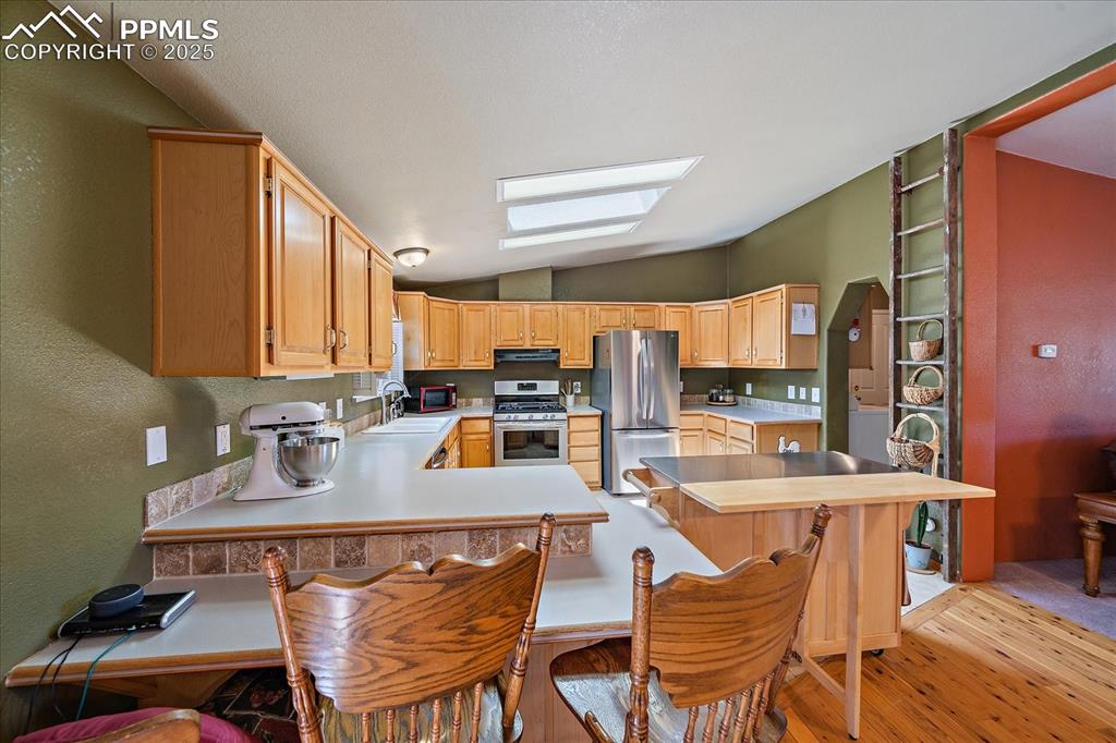 Image 11 of 50: Kitchen featuring light countertops, vaulted ceiling, a breakfast bar area,