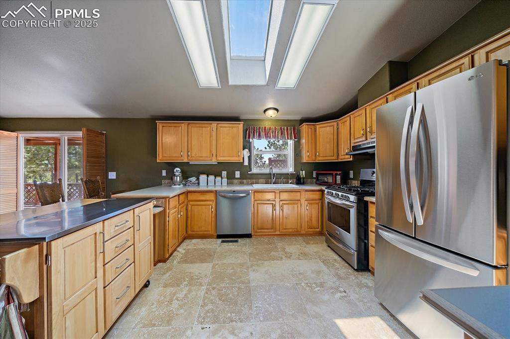 Image 13 of 50: Kitchen featuring stainless steel appliances, a skylight, dark countertops,