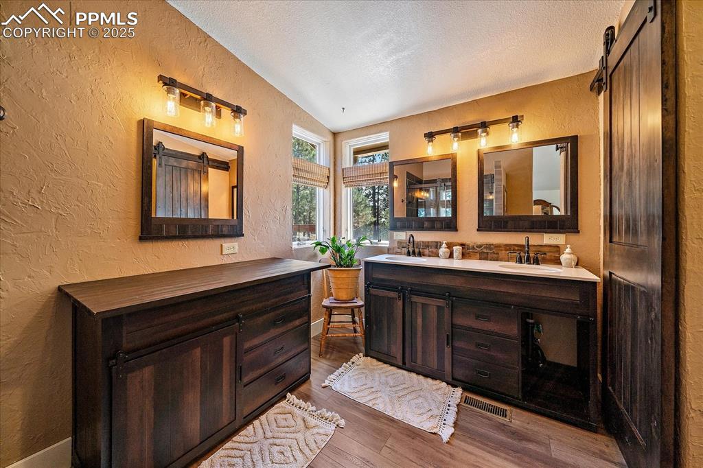 Image 17 of 50: Full bath featuring a textured wall, double vanity, dark wood finished floo
