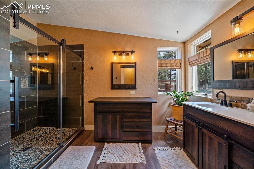 Image 18 of 50: Bathroom with a textured wall, two vanities, a shower stall, dark wood fini