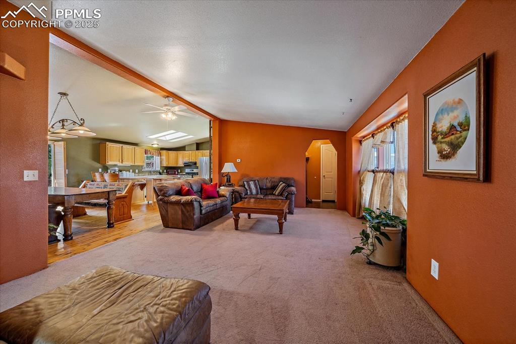 Image 7 of 50: Living room with light colored carpet, a ceiling fan, and a textured wall