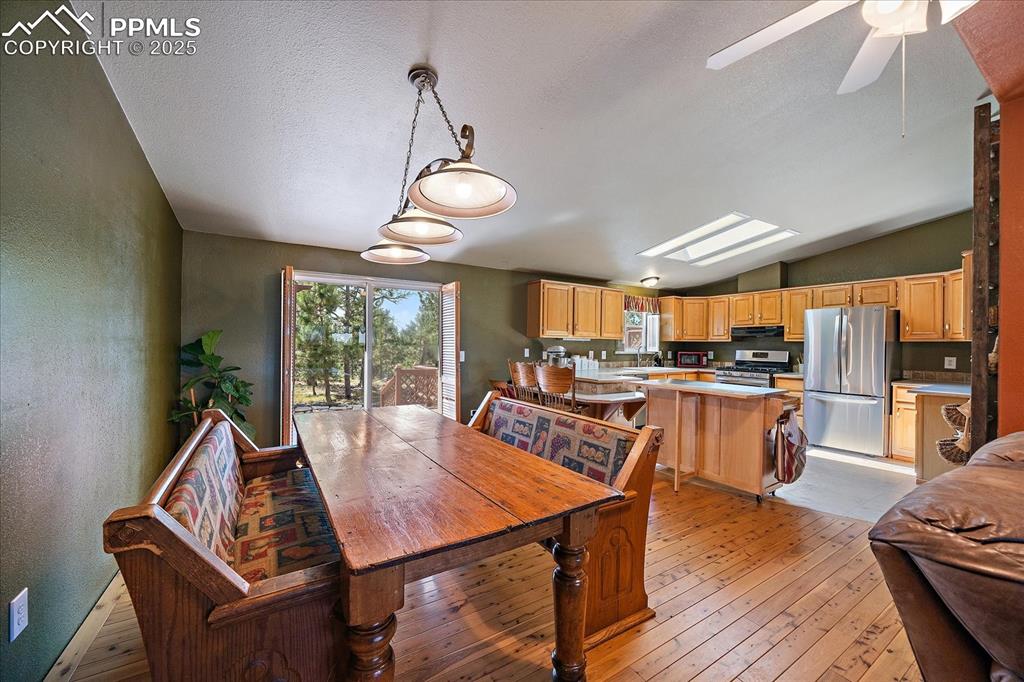 Image 8 of 50: Dining space with light wood-style flooring, vaulted ceiling, a textured wa