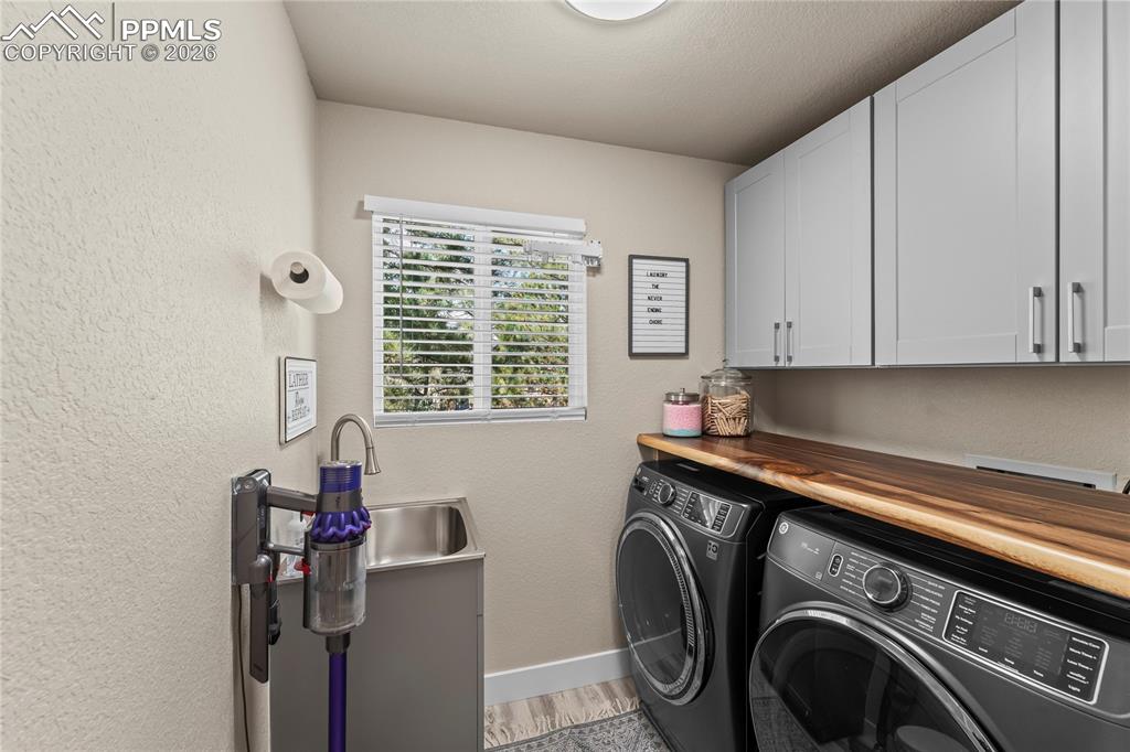 Image 35 of 44: Washroom featuring washer and dryer, cabinet space, a textured wall, and li