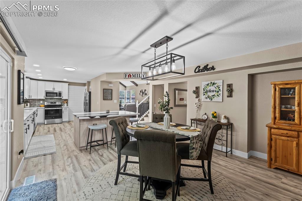 Image 9 of 44: Dining room featuring light wood finished floors, stairs, a textured ceilin