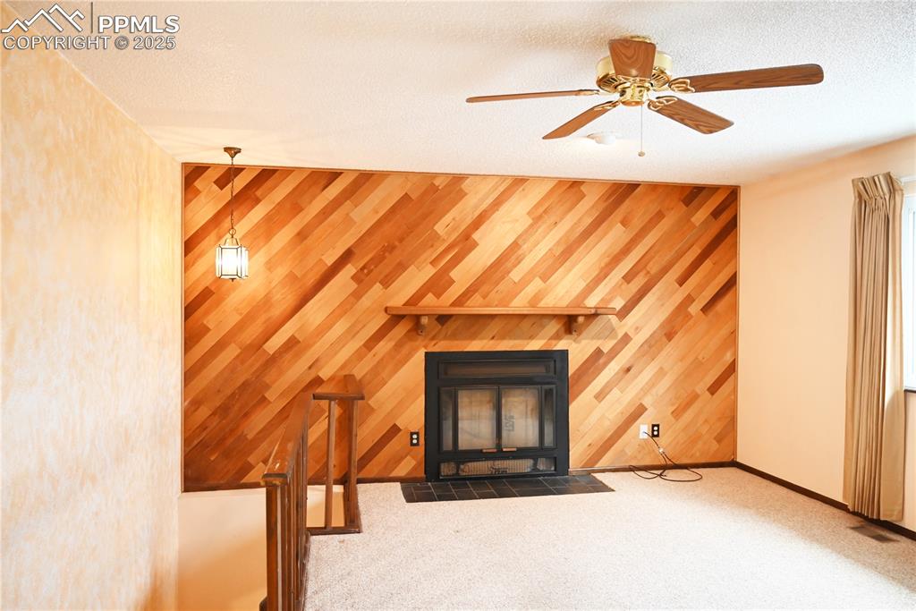 Image 10 of 17: Unfurnished living room with wood walls, a ceiling fan, and carpet floors