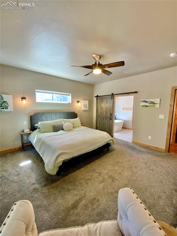 Image 14 of 47: Carpeted primary bedroom with a barn door, a ceiling fan, and ensuite bathr