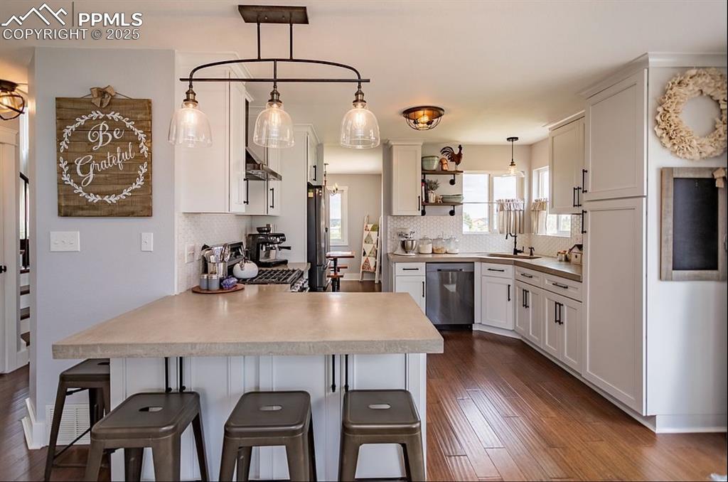 Image 11 of 44: Kitchen featuring a peninsula, decorative light fixtures, white cabinets, b