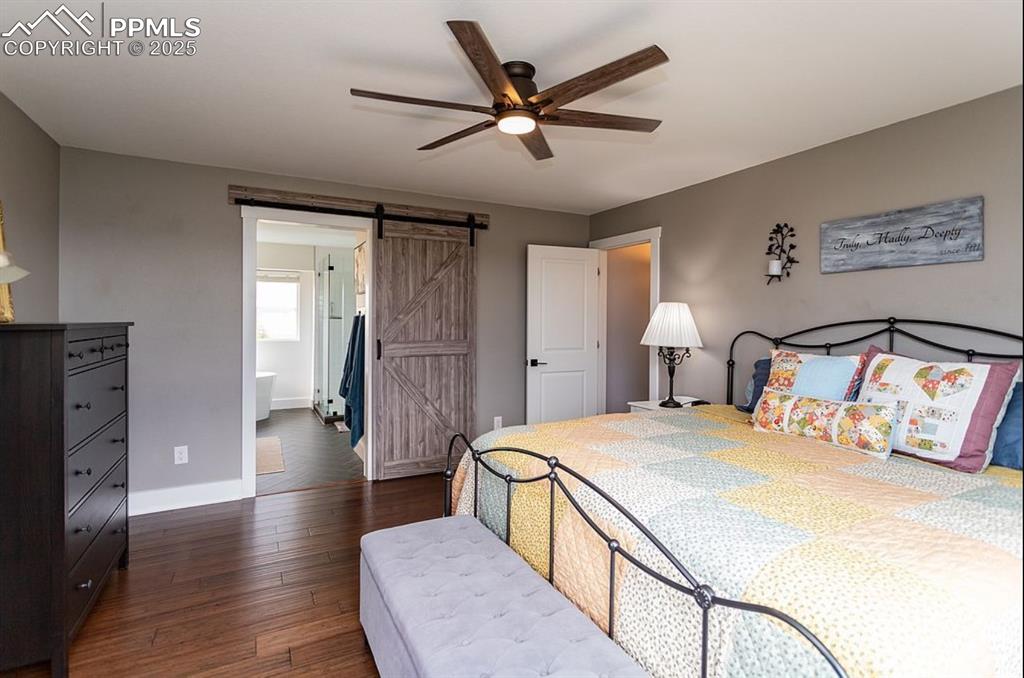 Image 19 of 44: Bedroom featuring dark wood-type flooring, a barn door, ceiling fan, and en