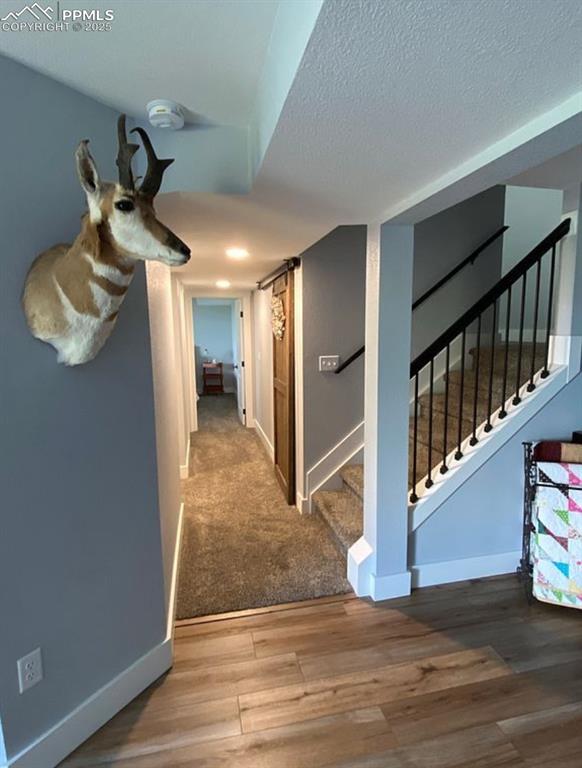 Image 24 of 44: Corridor with stairway, a barn door, a textured ceiling, wood finished floo