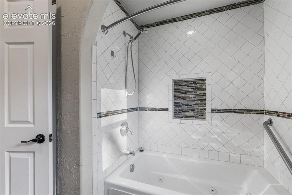 Image 18 of 32: Bathtub with integrated jets, diamond-patterned tile surround, decorative m