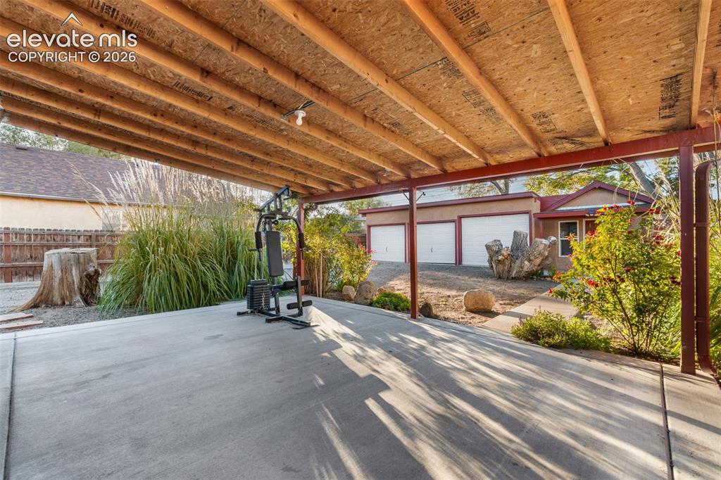 Image 21 of 32: Covered concrete patio with exposed timber joist ceiling and steel support 
