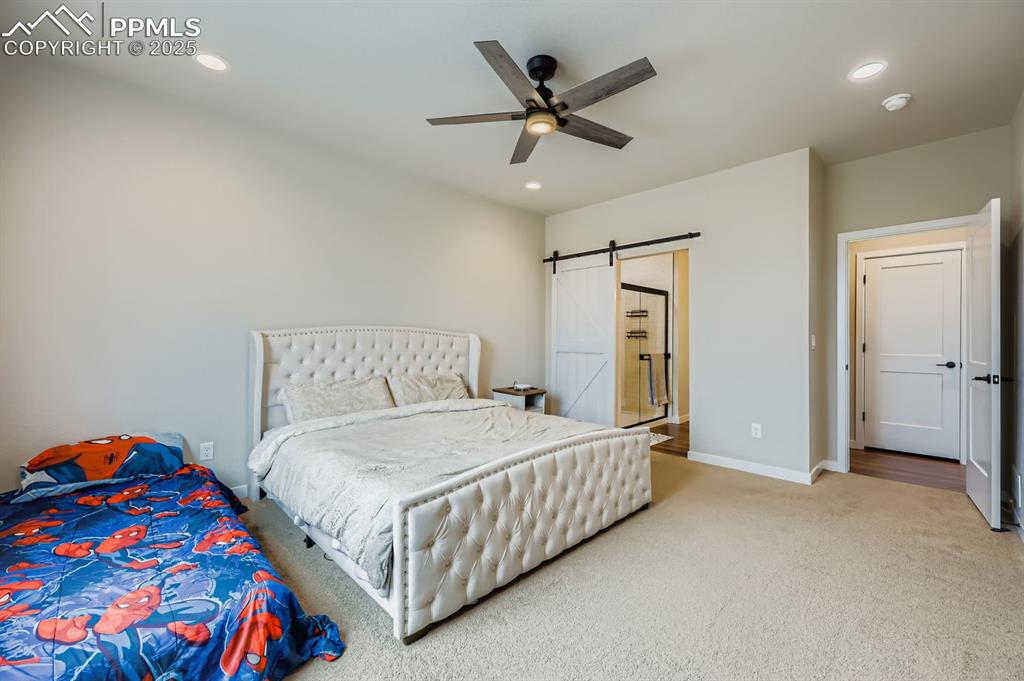 Image 12 of 28: Carpeted bedroom with a barn door, ensuite bath, recessed lighting, and a c